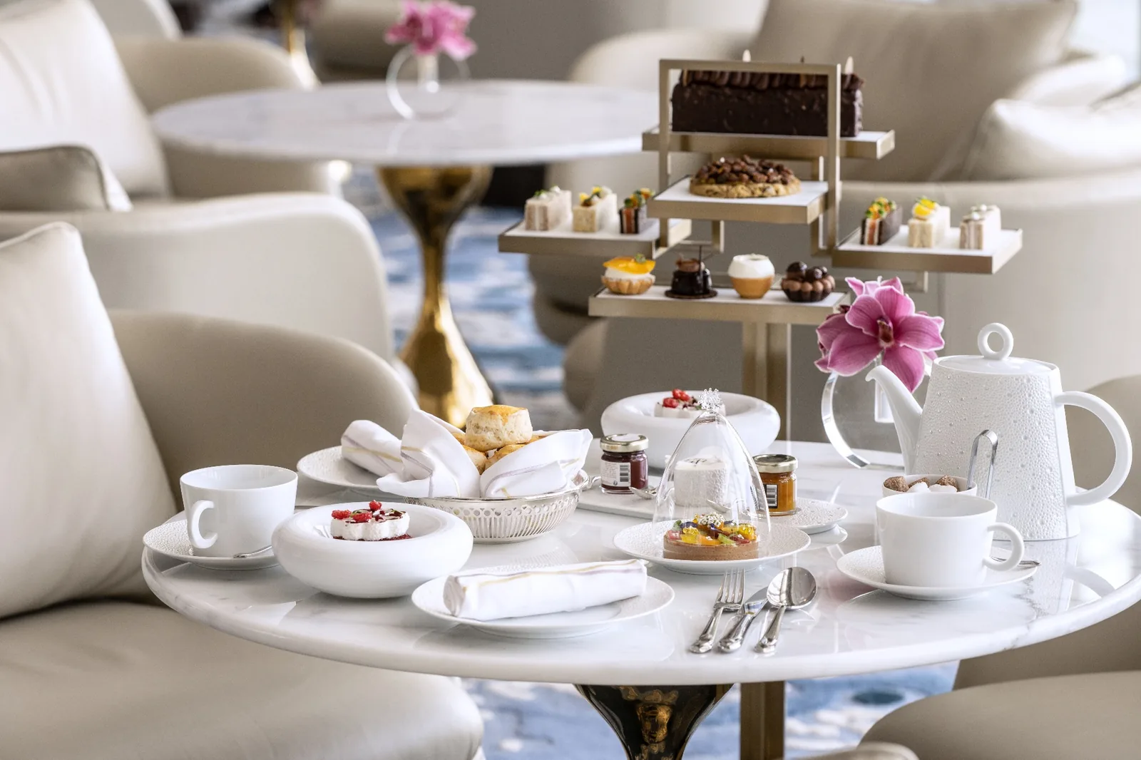 Afternoon tea service at Atlantis The Royal: a marble table set with scones, pastries and a white teapot beside a tiered stand of savouries and cakes
