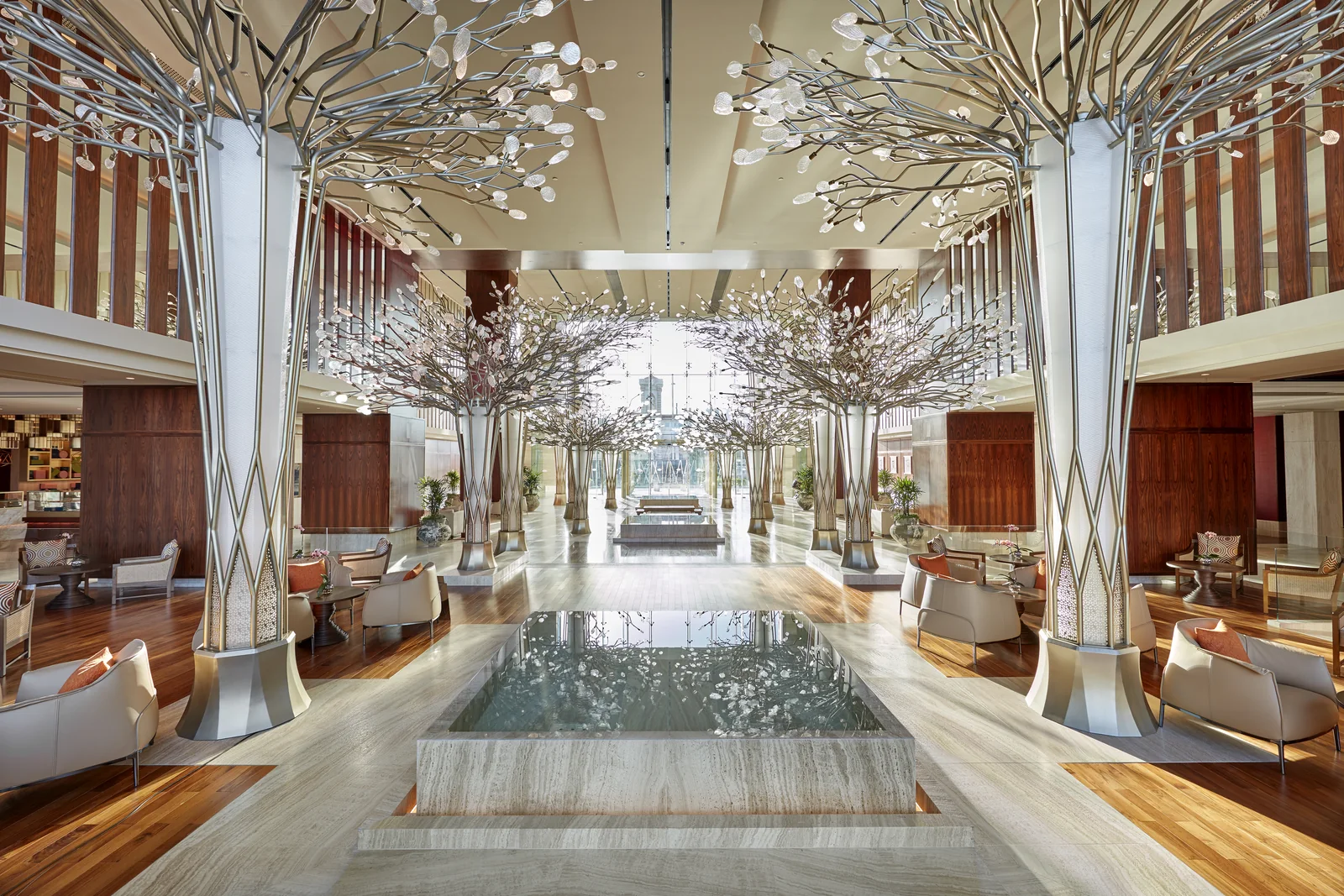 The lobby at Mandarin Oriental Jumeira, Dubai, a double-height hall with sculptural metal trees, a reflecting pool and armchair seating