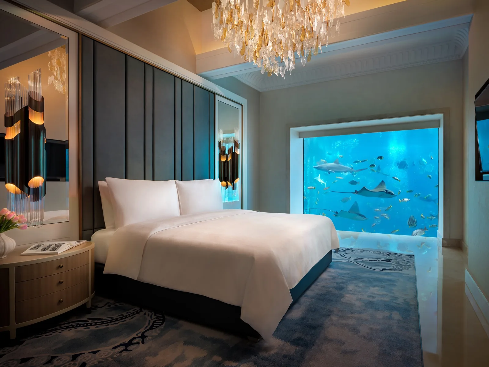 A suite bedroom at Atlantis, The Palm with a king bed and a floor-to-ceiling window onto an aquarium with sharks and rays