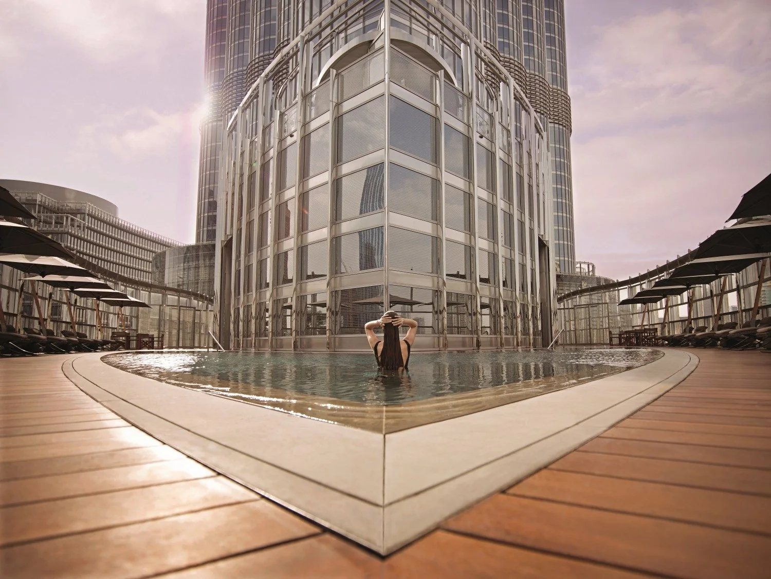 An outdoor pool on a timber deck with loungers and parasols at the base of the Burj Khalifa