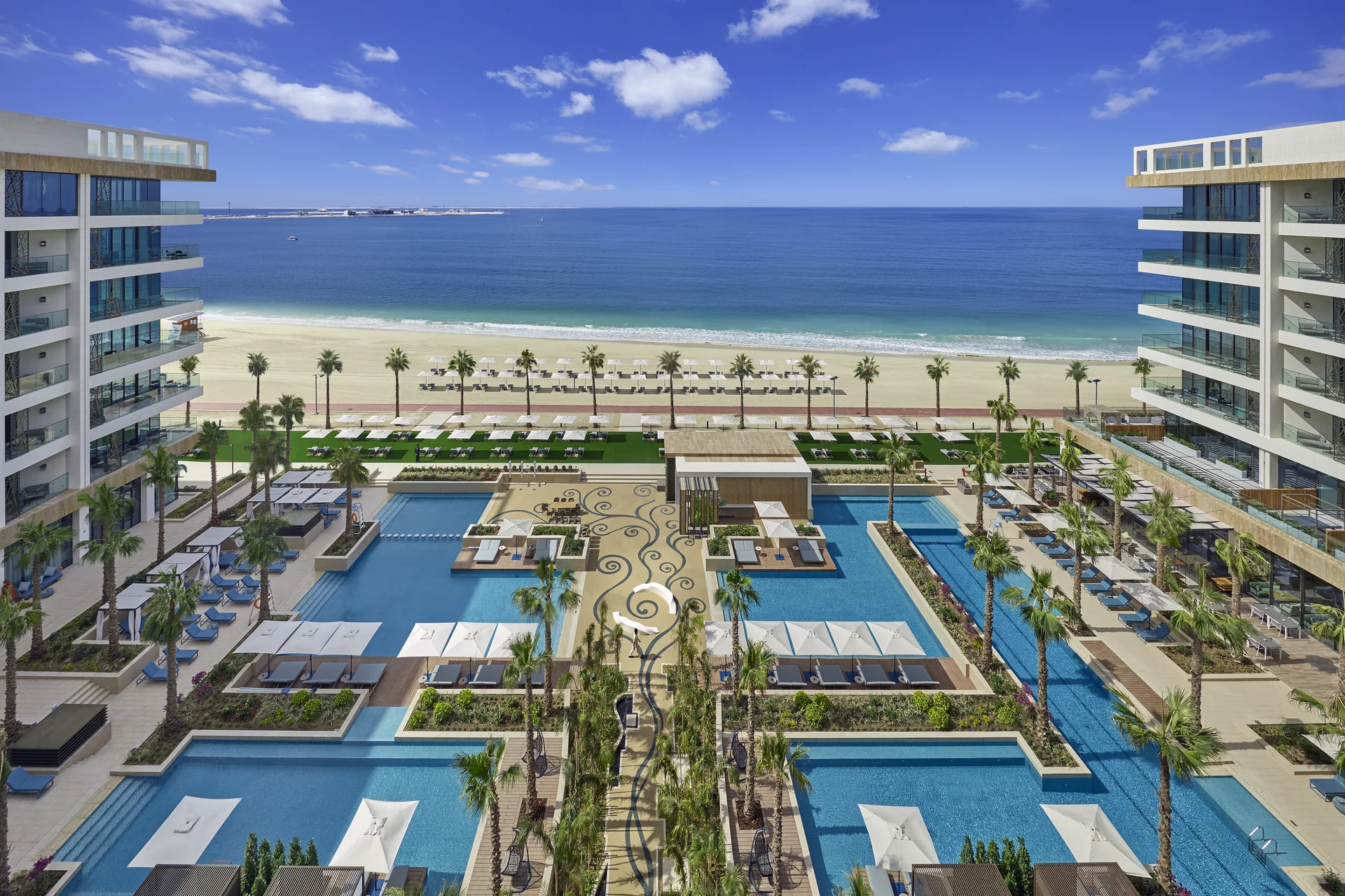 Mandarin Oriental Jumeira, Dubai seen from above: palm-lined pools and terraces between two white wings, with the beach and sea beyond