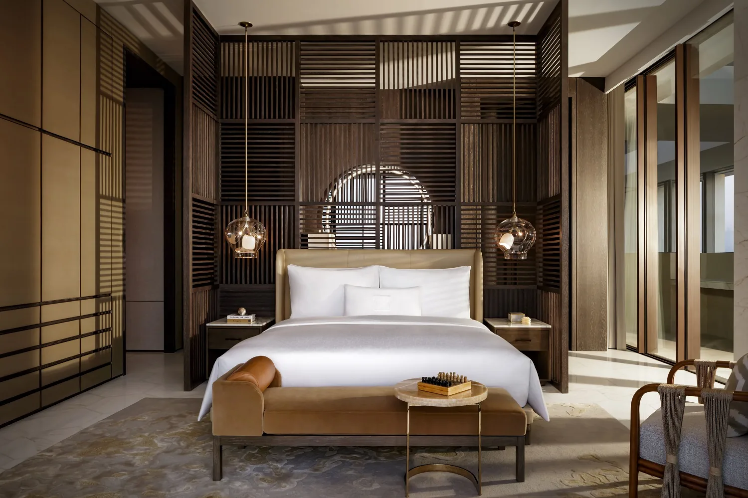 A suite bedroom at Atlantis The Royal with a king bed, timber screen headboard wall, glass pendant lights and a tan leather chaise