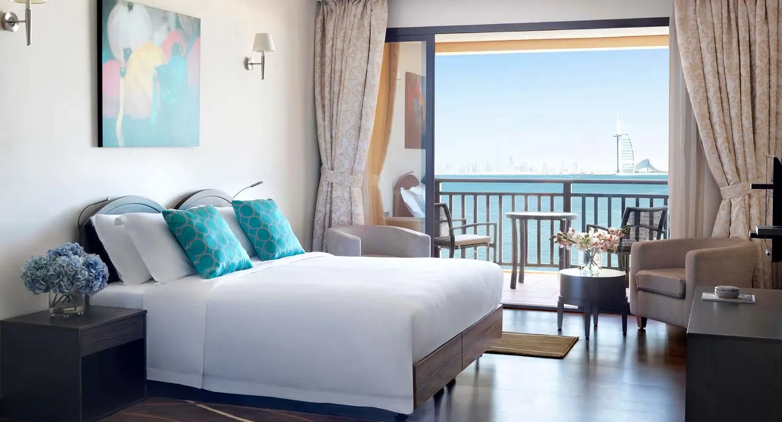 A guest room at Anantara The Palm Dubai Resort with a king bed, turquoise cushions and sliding doors onto a sea-view balcony