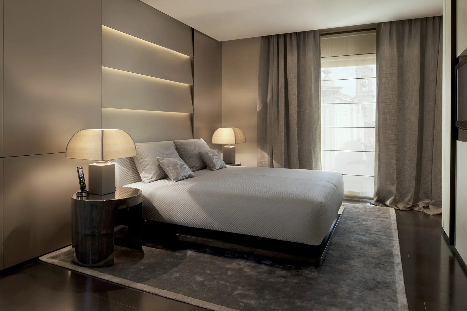 A guest room at Armani Hotel Dubai with a low platform bed, backlit panelled headboard wall, table lamps and linen curtains
