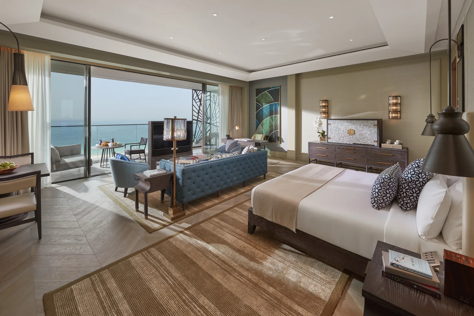 A guest room at Mandarin Oriental Jumeira, Dubai with a king bed, blue tufted sofa and sliding doors onto a sea-view balcony