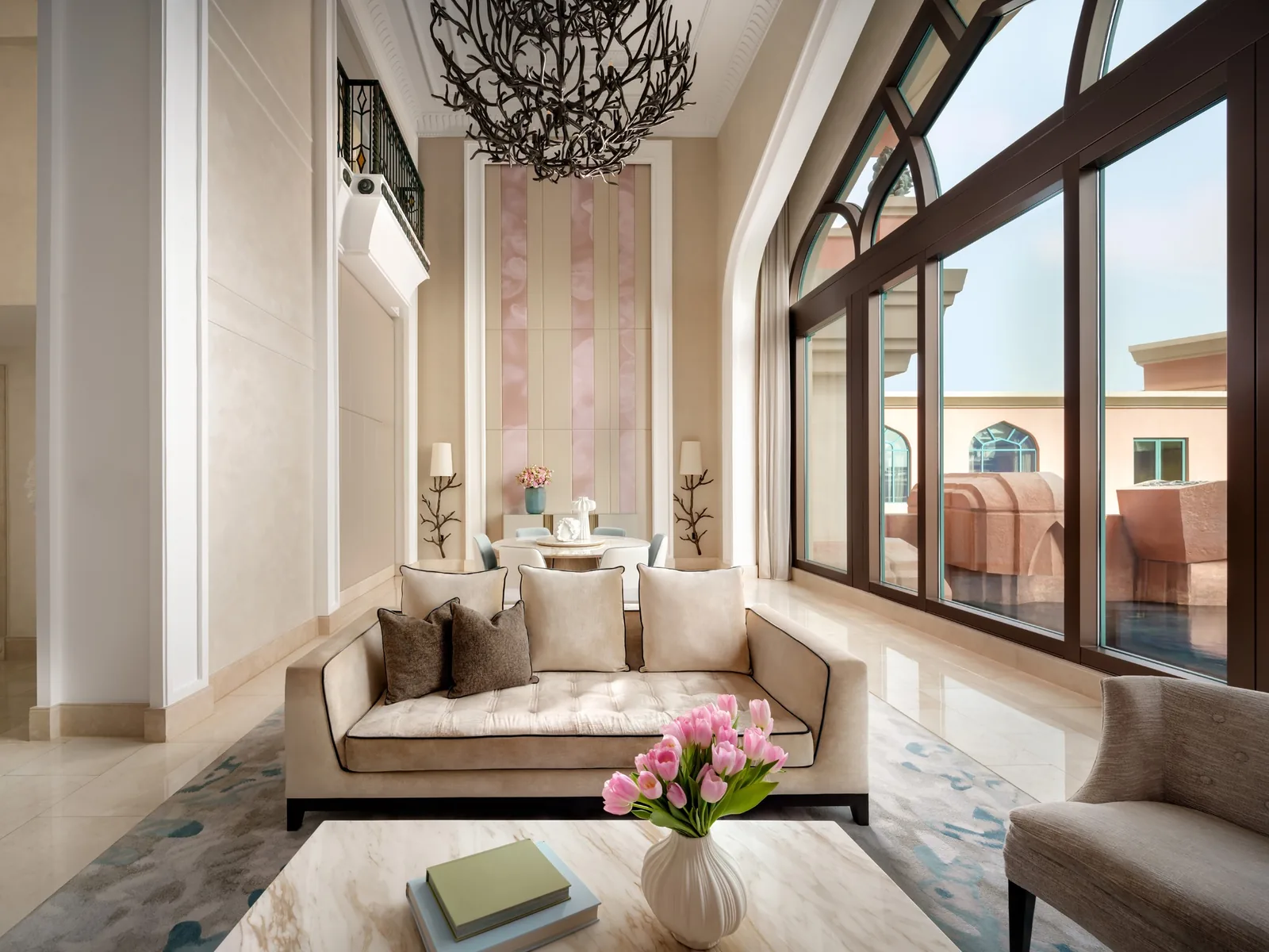 A double-height suite living room at Atlantis, The Palm with a cream sofa, branch chandelier and tall arched windows